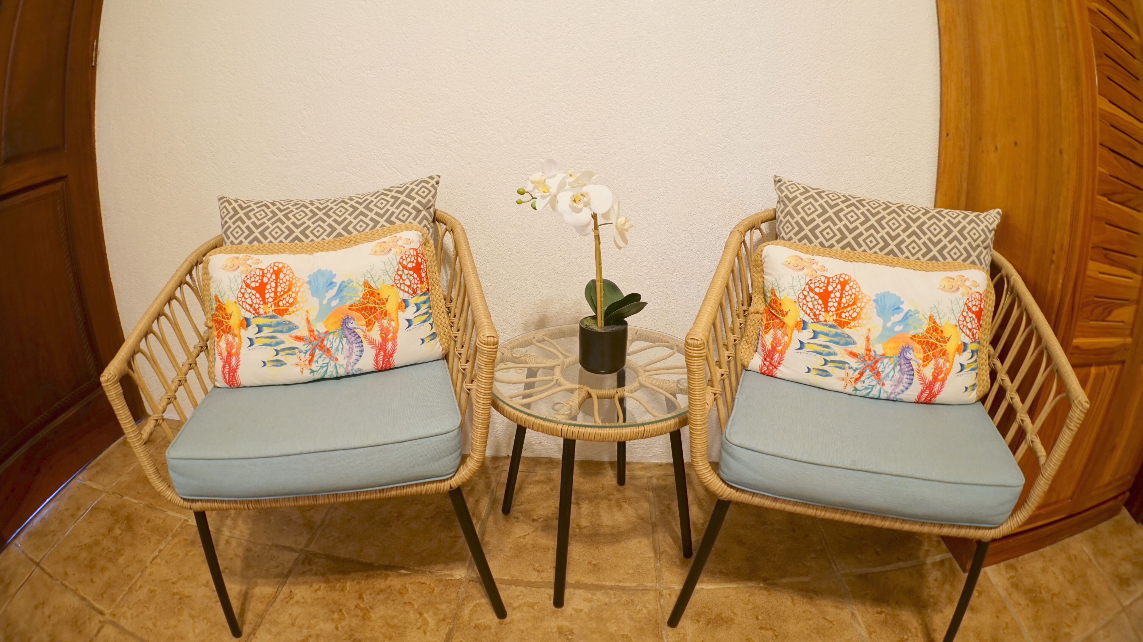 Two wicker chairs with patterned cushions and a small table with a potted orchid between them.