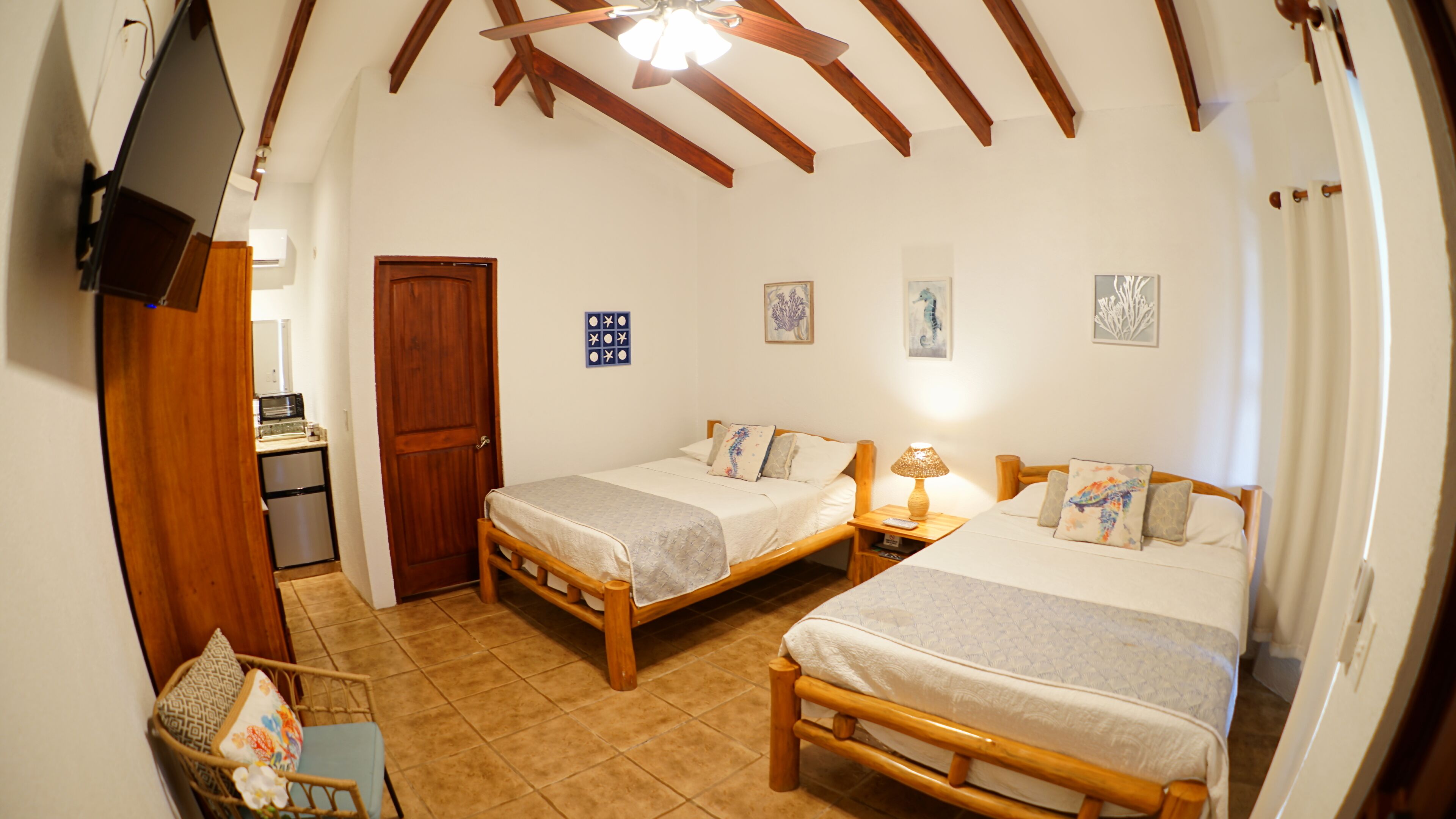 A room with two wooden beds, a small table, a chair, and a TV mounted on the wall.