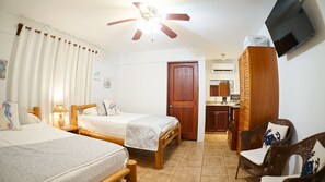 A hotel room with two single beds, a wooden wardrobe, a television, a ceiling fan, and a kitchenette. - Villas Welcome to Heaven (Puerto Carrillo)