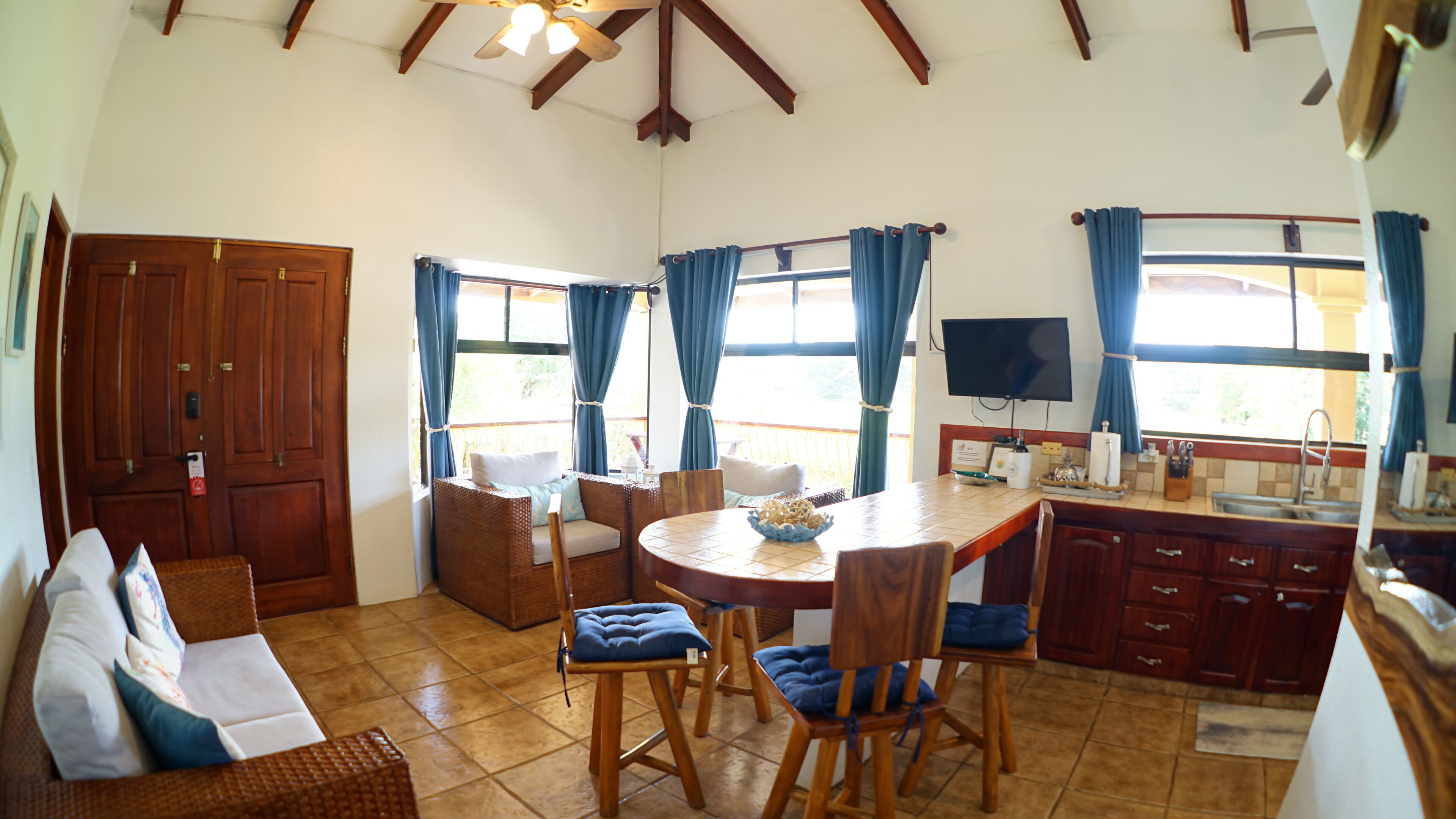 A spacious living area with a dining table, chairs, a sofa, and a kitchen area with a TV.