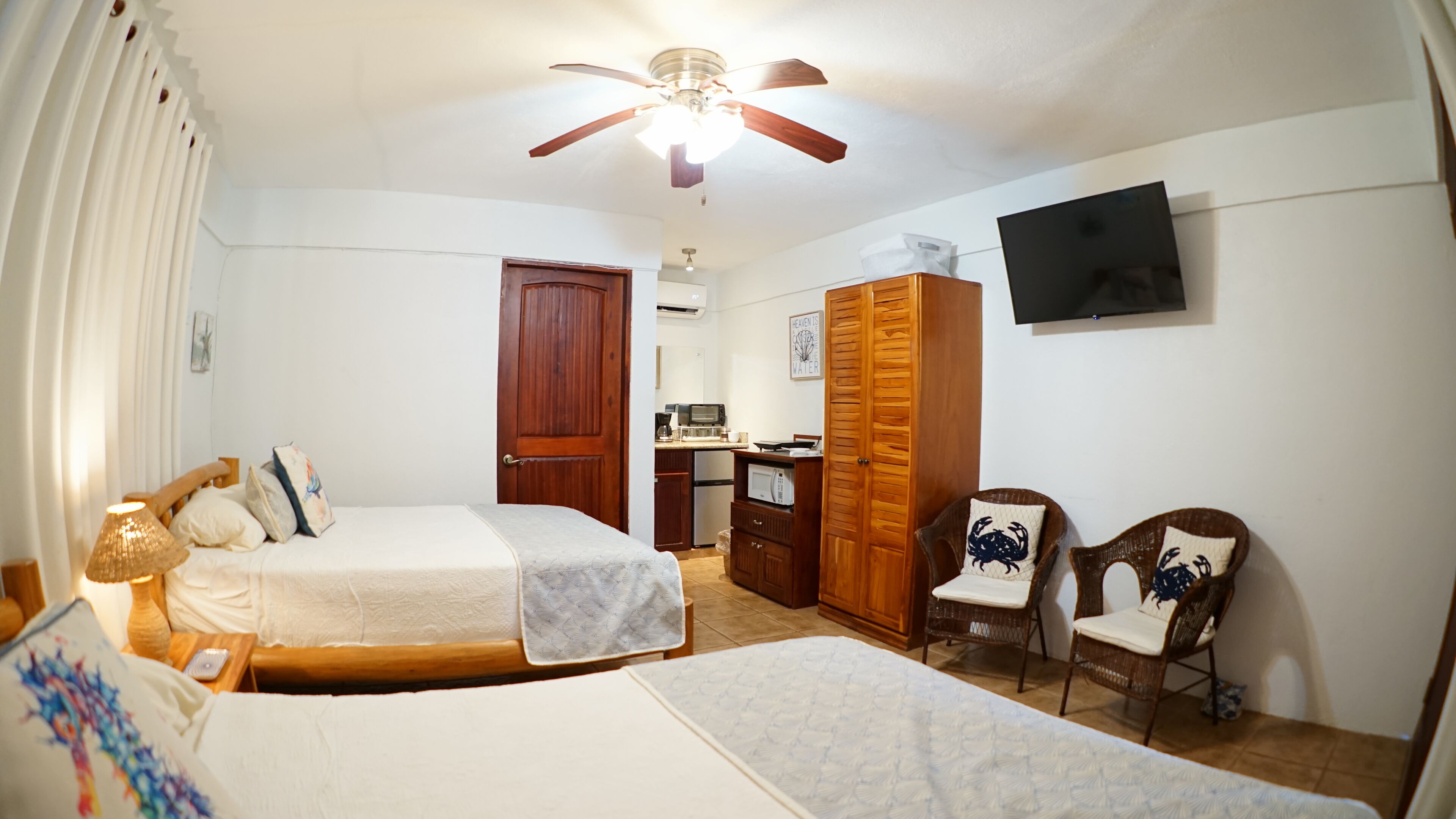 A bedroom with two beds, a wardrobe, a desk, and a television.