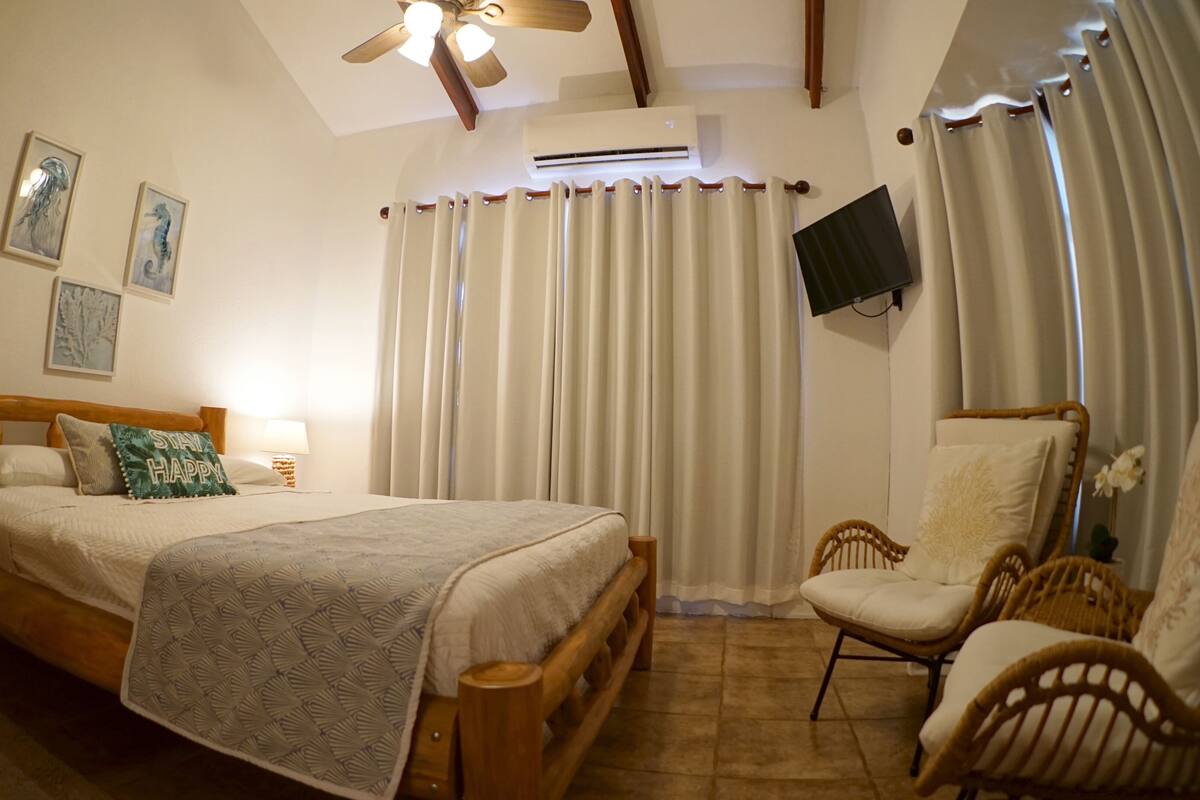 A bedroom with a bed, a chair, a TV, and a ceiling fan.