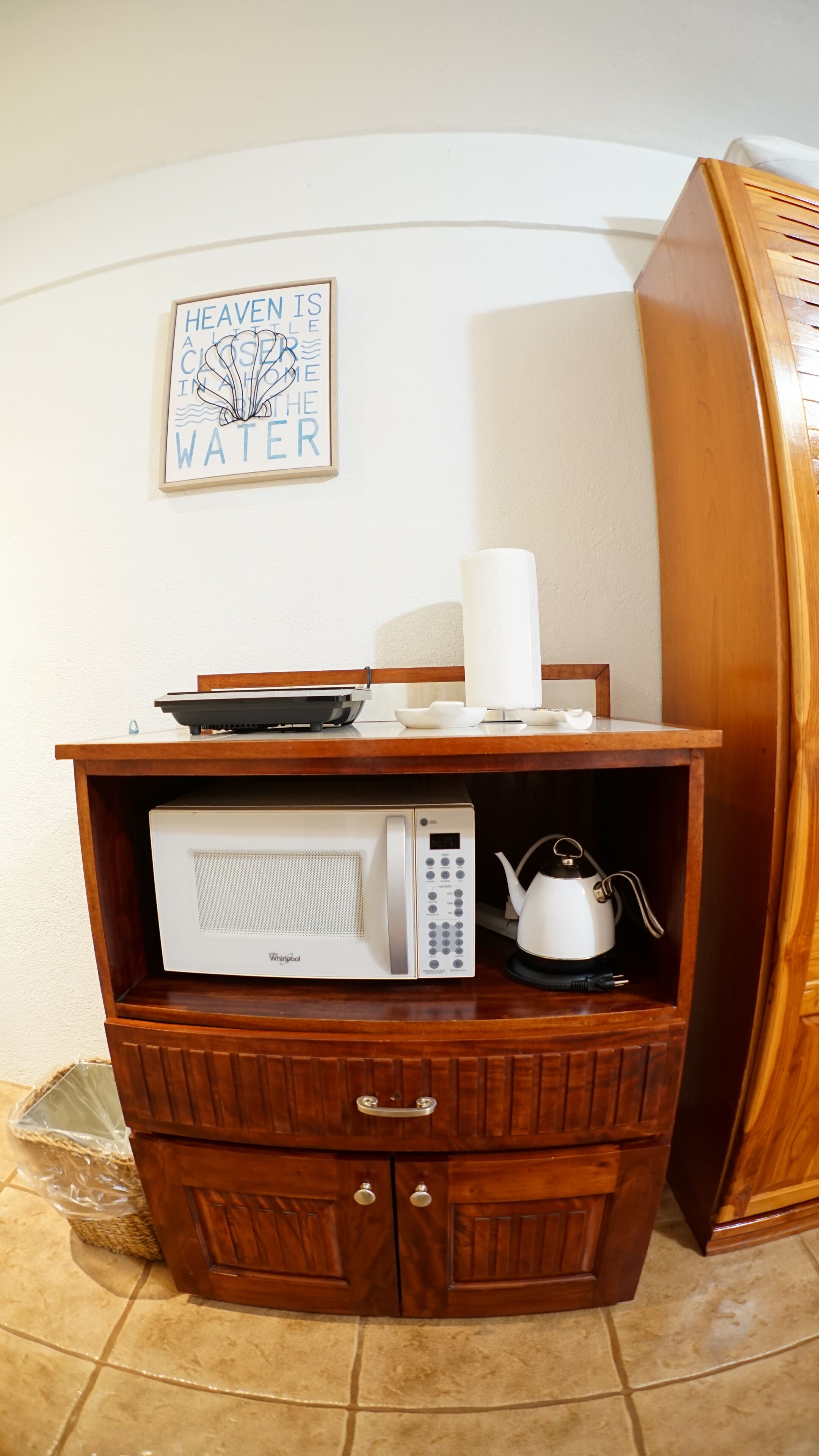 A kitchen area with a microwave, a kettle, and a framed quote on the wall.