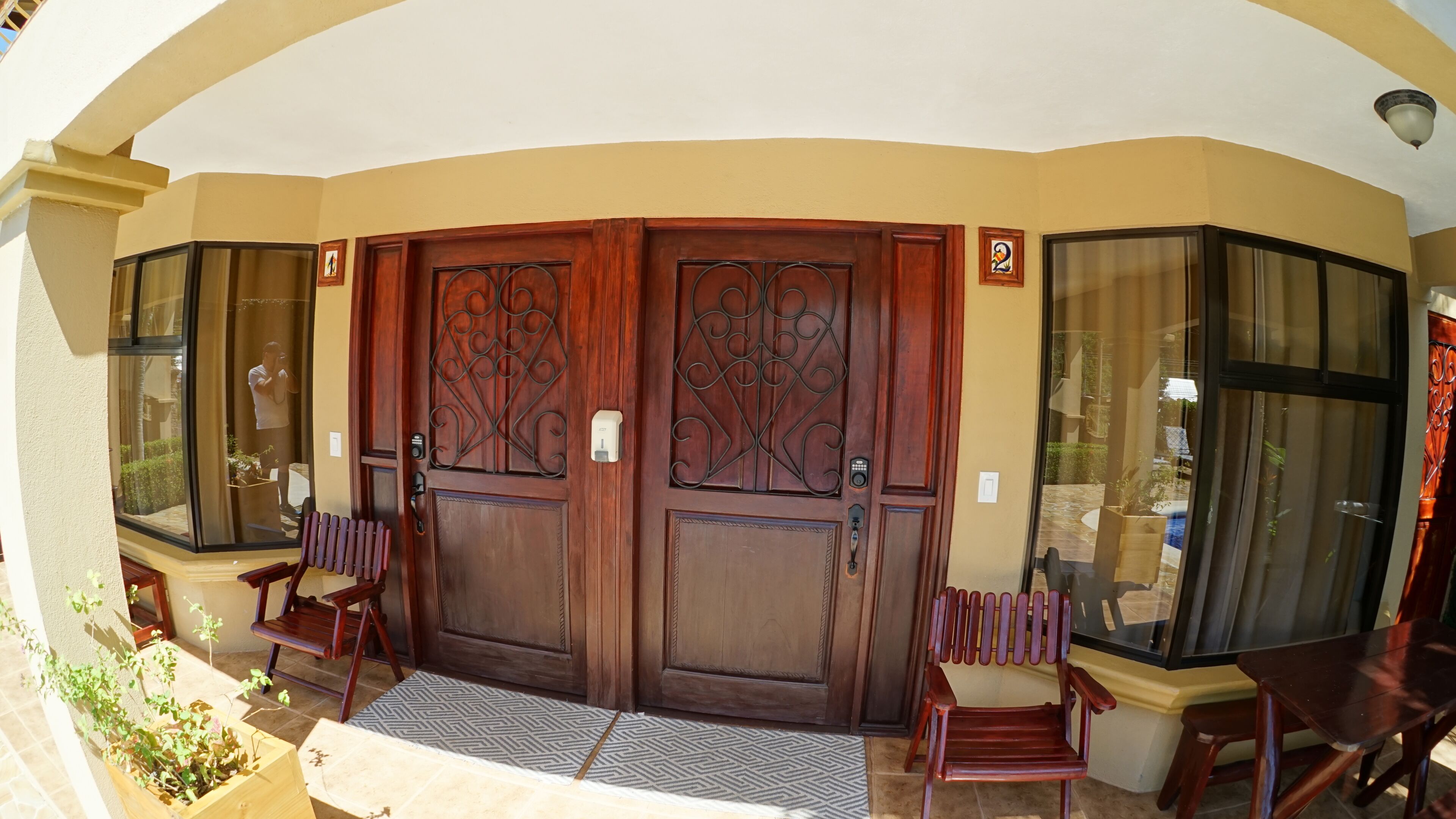 A set of double wooden doors with intricate metalwork, flanked by glass panels and two wooden chairs.