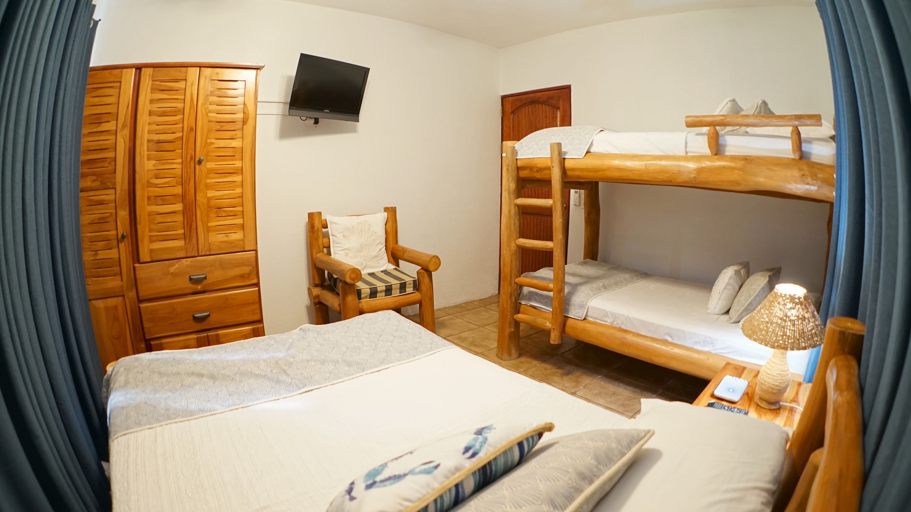 A room with bunk beds, a wooden wardrobe, a chair, a television, and a bedside lamp.