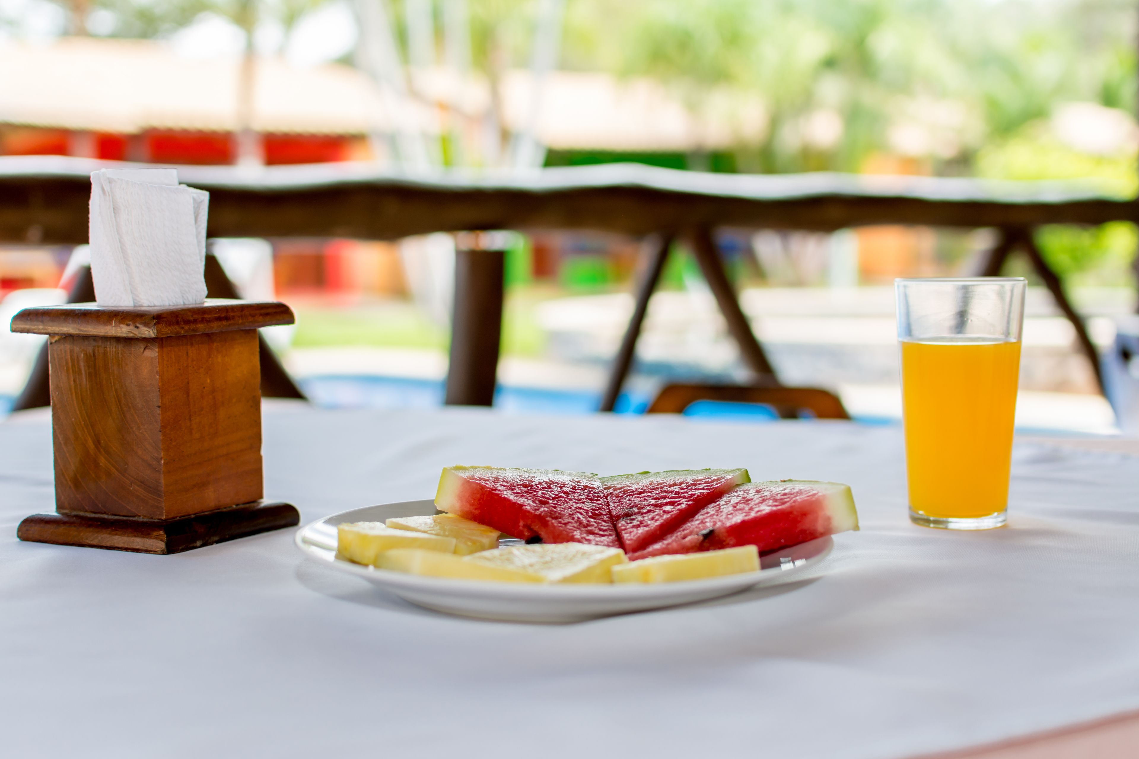 Una mesa con un plato de fruta, un vaso de jugo de naranja y un sujetador de servilletas.