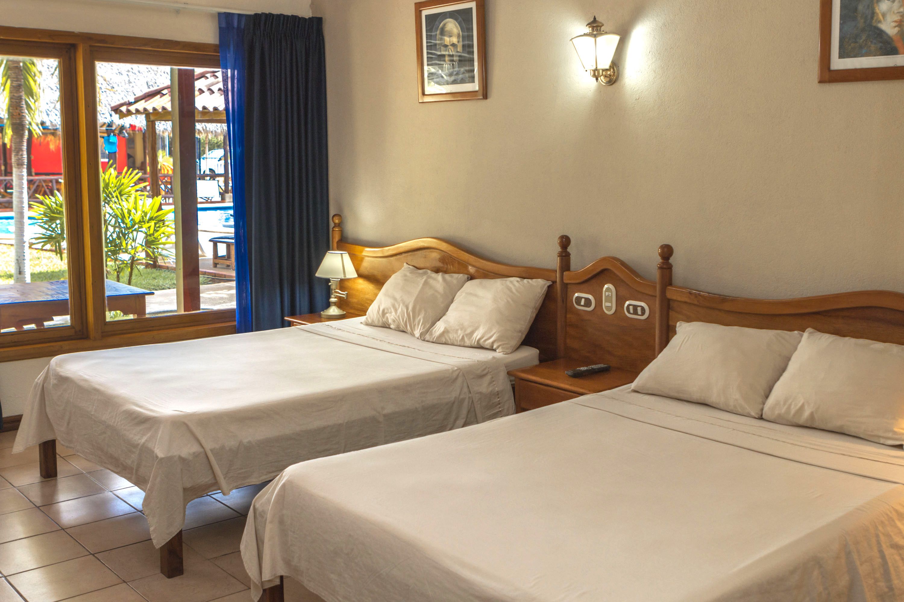 A hotel room with two beds, a window with a view of the pool, a lamp, and a painting on the wall.