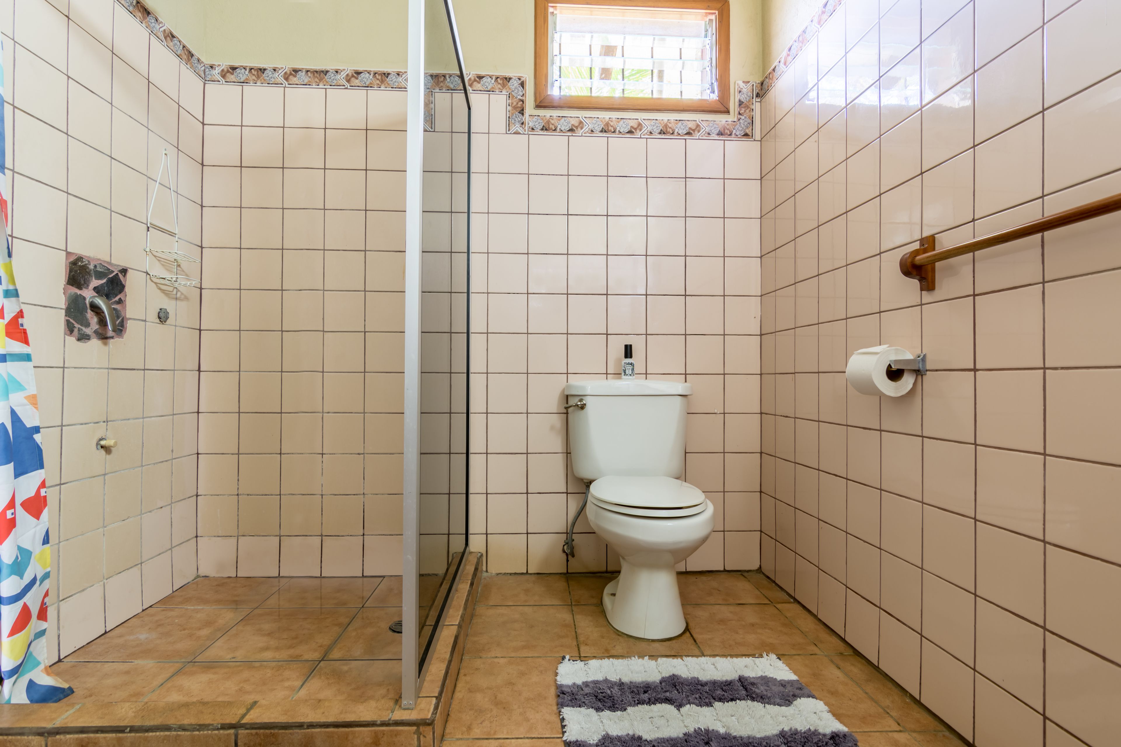 A bathroom with a toilet, shower, and a small window.