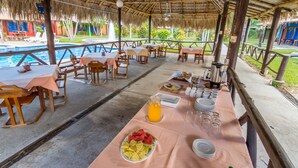 A covered dining area with tables and chairs, a pool in the background, and a tropical setting. - Guanacaste Lodge (Cabo Velas)