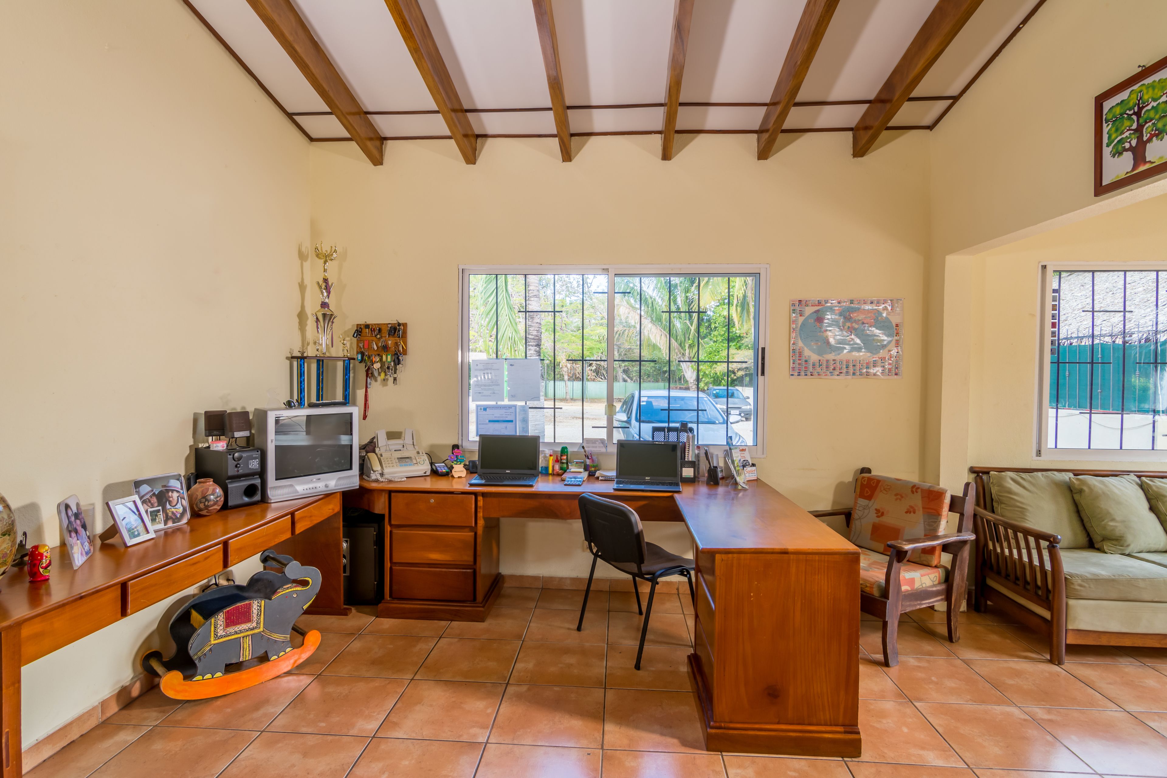 A spacious living area with a wooden desk, two laptops, a chair, a sofa, and a rocking horse.