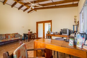 A spacious living room with a wooden ceiling, a sofa, a dining table, and a TV.