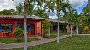 A row of colorful, single-story buildings with a red and green facade, surrounded by palm trees and a well-maintained lawn. - Guanacaste Lodge (Cabo Velas)