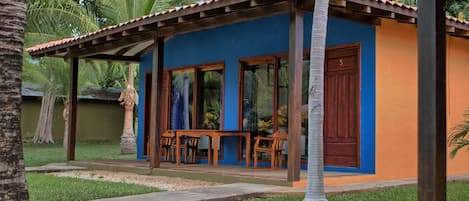 A small, single-story building with a blue and orange exterior, wooden furniture, and a tiled roof.