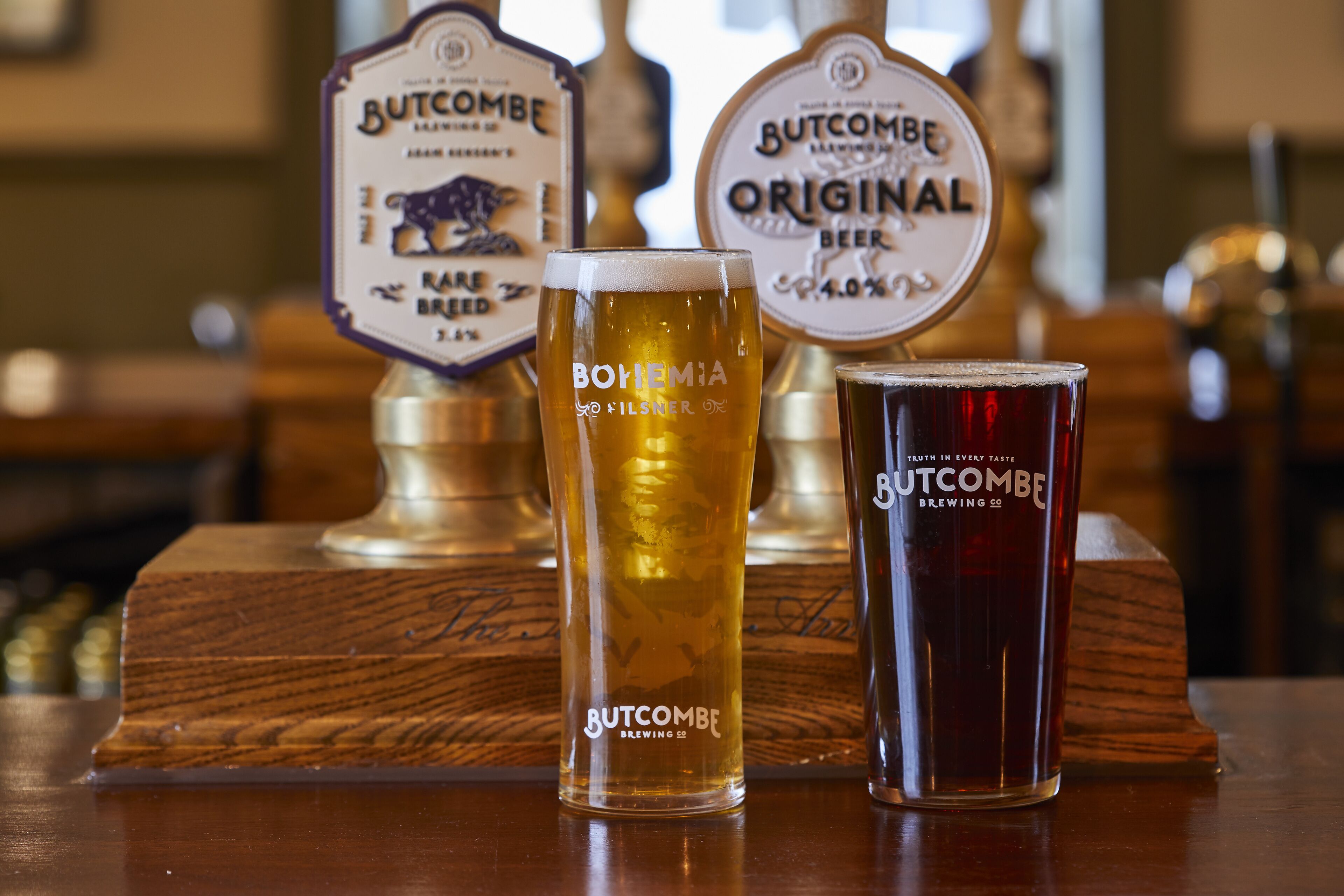 Deux tireuses à bière portant les inscriptions « Butcombe » et « Butcombe Original », avec un verre de bière placé entre les deux.
