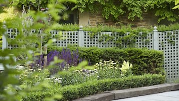 A garden with a white picket fence, various plants, and a stone wall in the background.