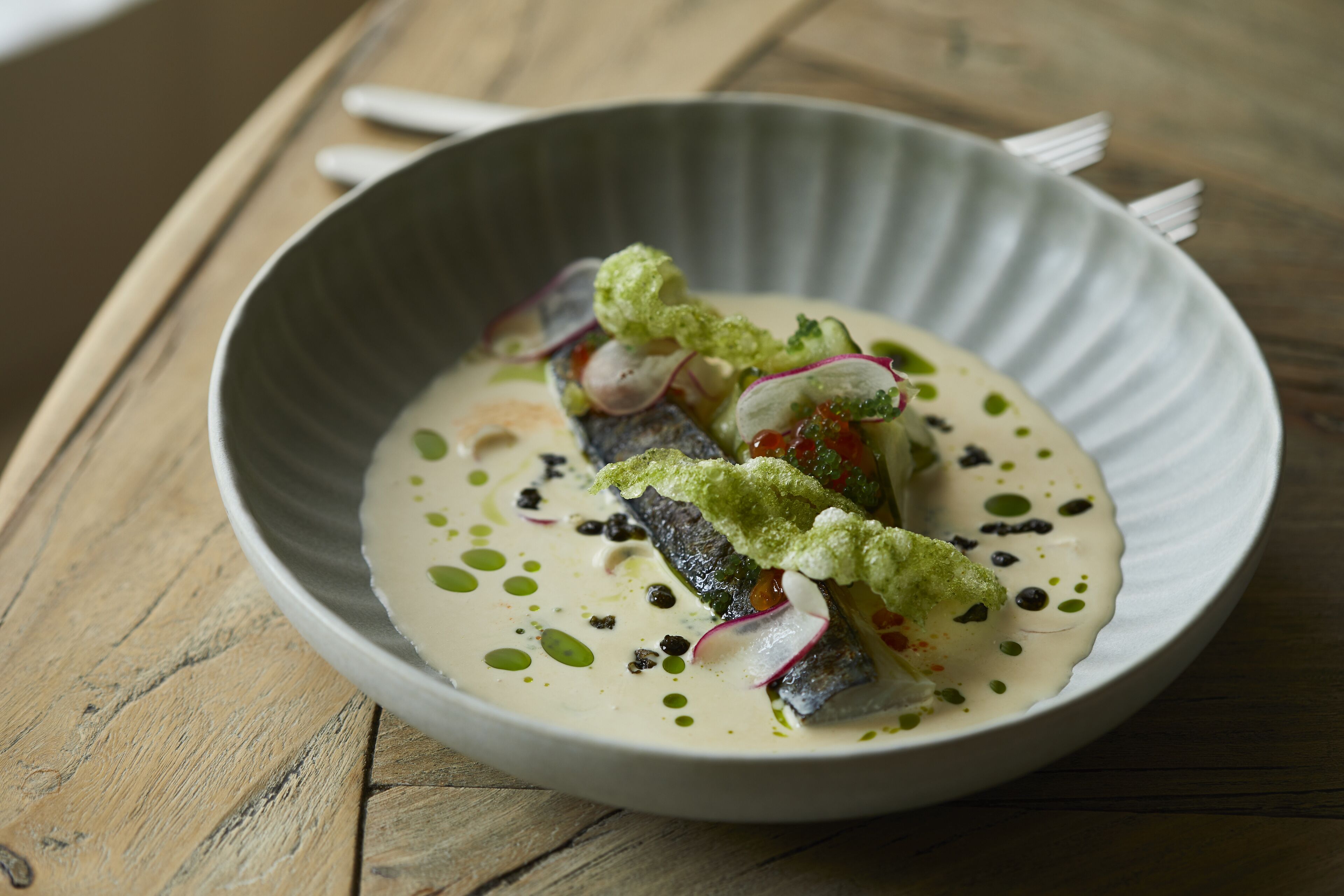 Un plato de comida con pescado, verduras y salsa sobre una mesa de madera.