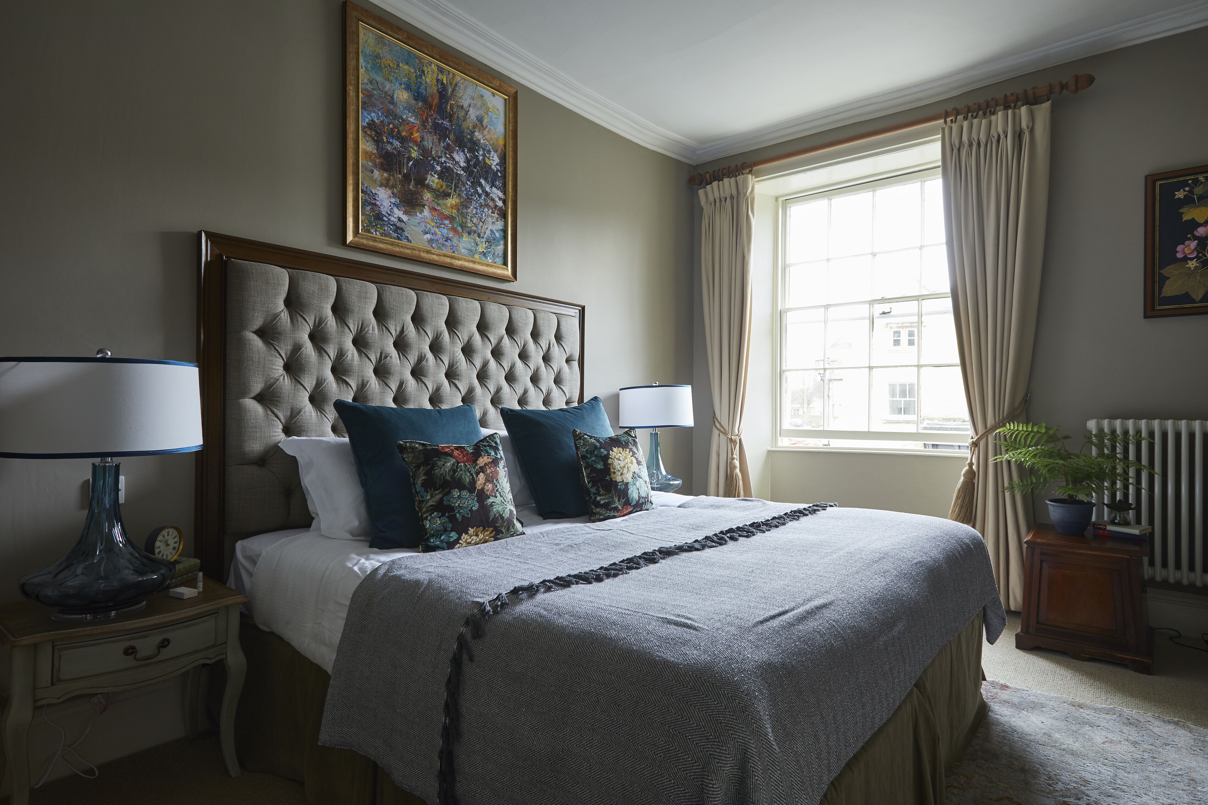 A neatly made bed with a tufted headboard, two bedside lamps, and floral pillows.