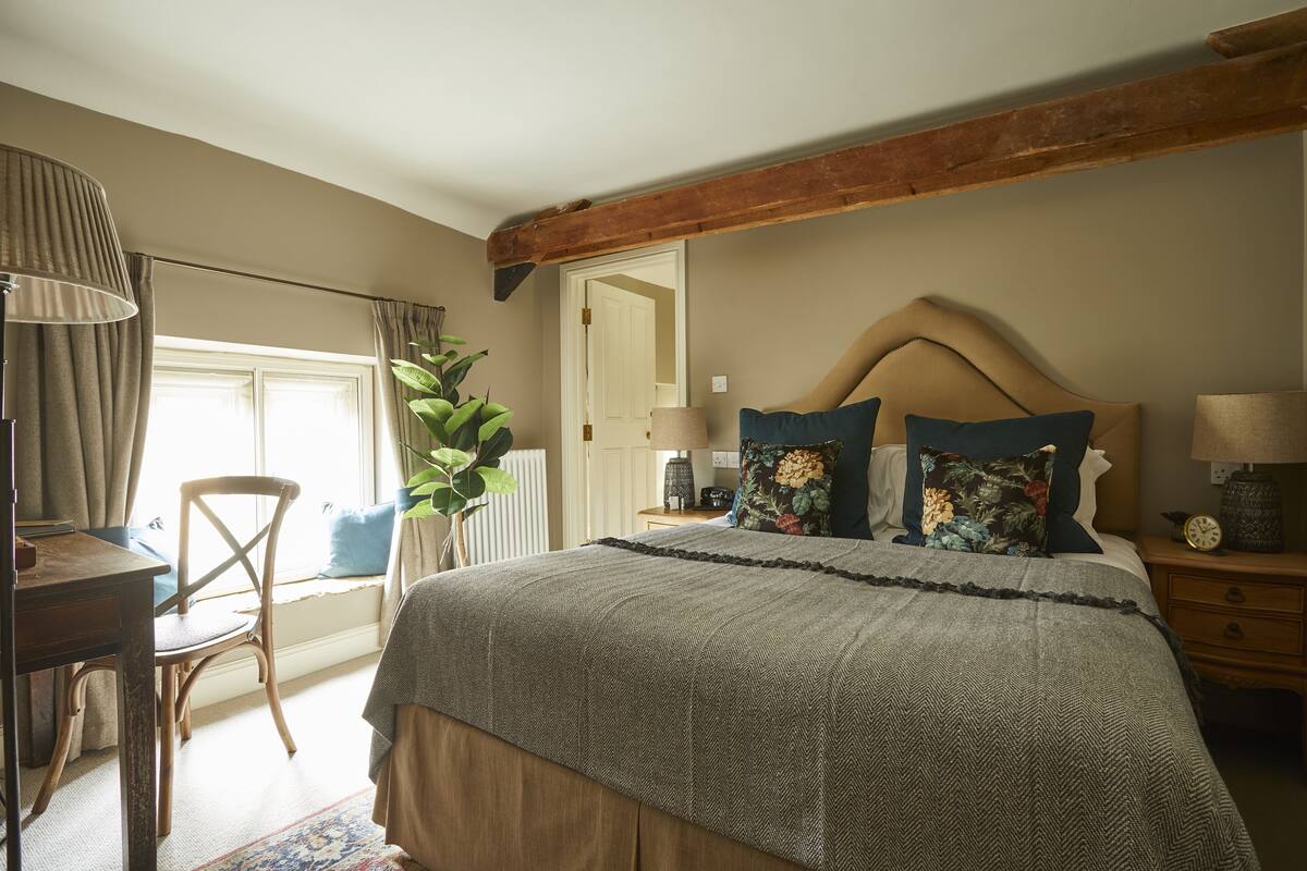 A bedroom with a large bed, wooden headboard, bedside tables with lamps, a chair, and a window with curtains.