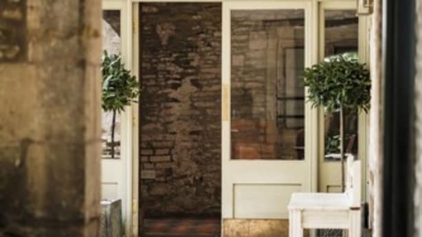 A stone wall, a wooden door, and a white chair in a hallway. - Methuen Arms (Corsham)