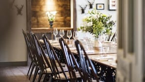 A dining area with a long table set for a meal, wooden chairs, and a vase of flowers. - Methuen Arms (Corsham)