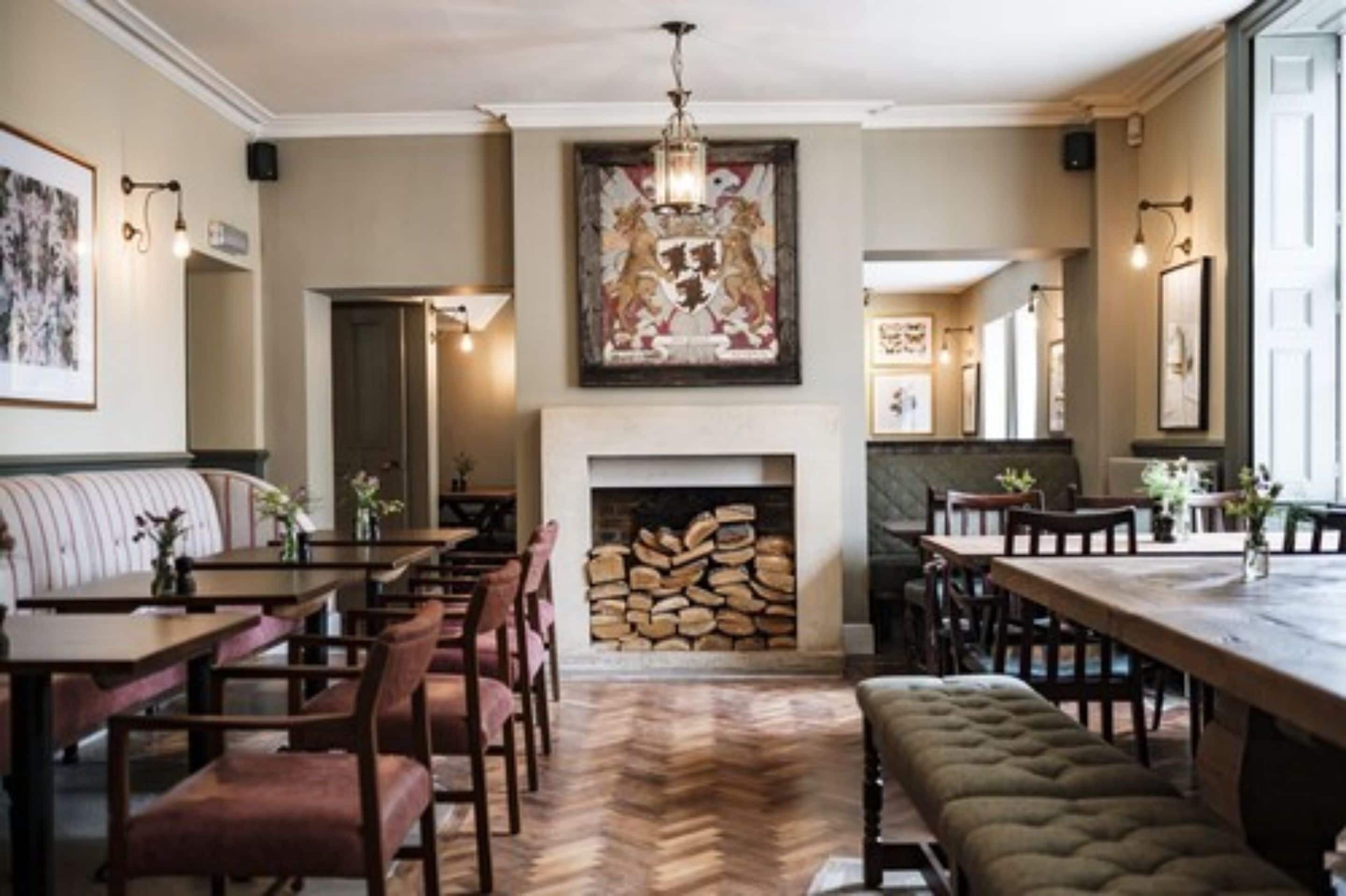 A dining area with wooden tables and chairs, a fireplace, and a large painting on the wall.