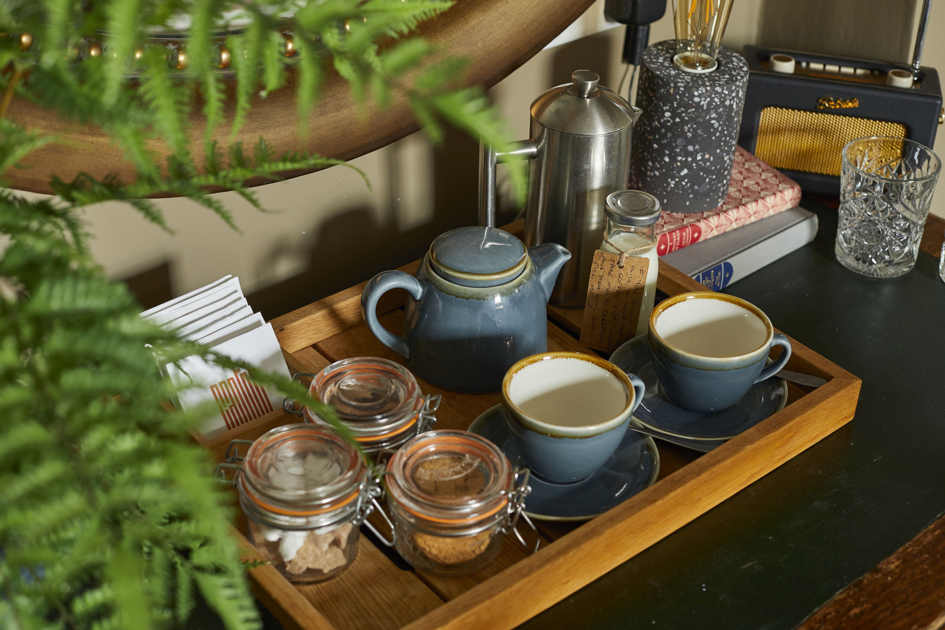 A tray with a teapot, cups, and jars of tea on a wooden surface.