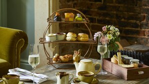 A three-tiered tea service with pastries, a teapot, cups, and a glass of wine on a wooden table. - Methuen Arms (Corsham)