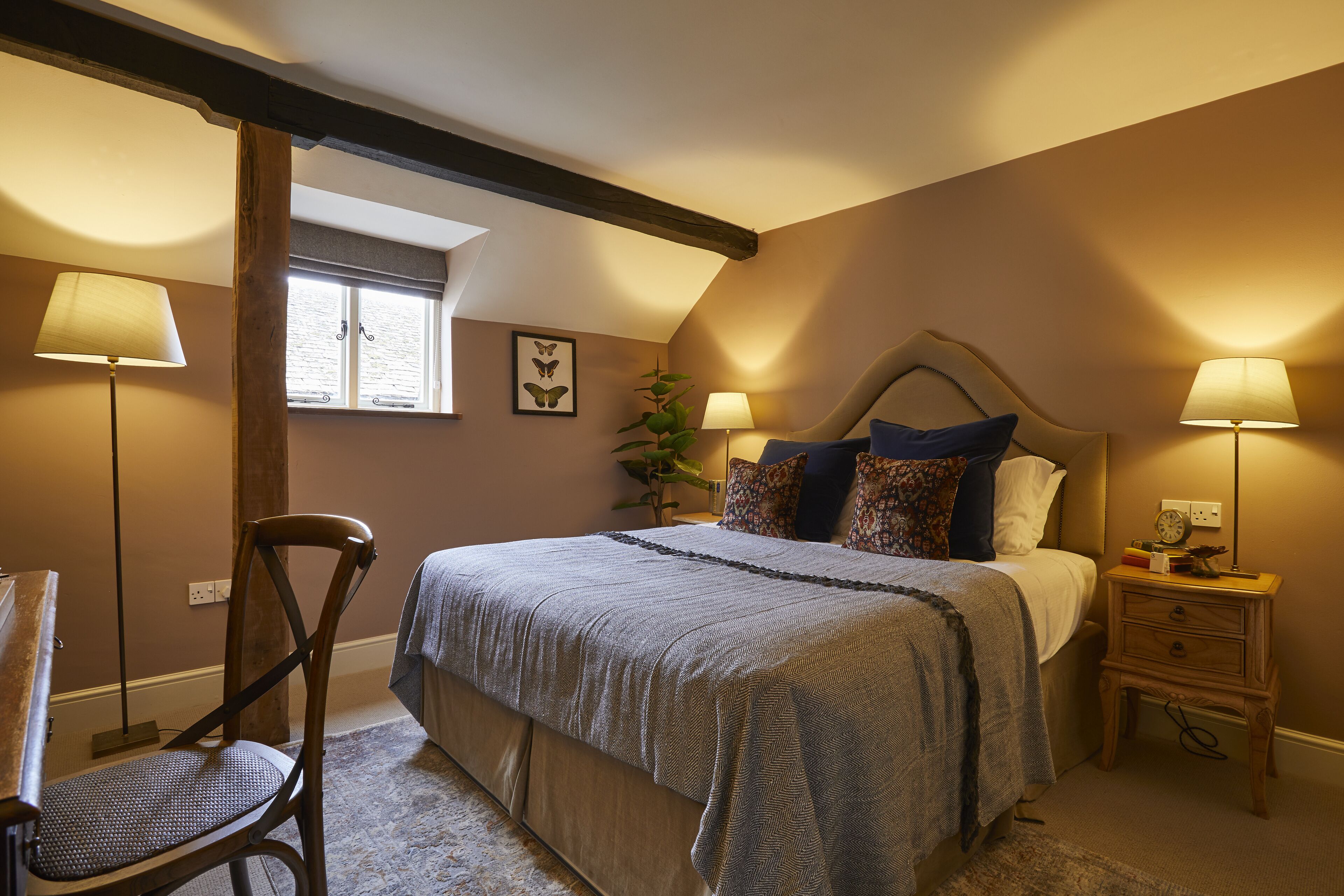 A bedroom with a large bed, two bedside tables with lamps, a chair, a window, and a plant.