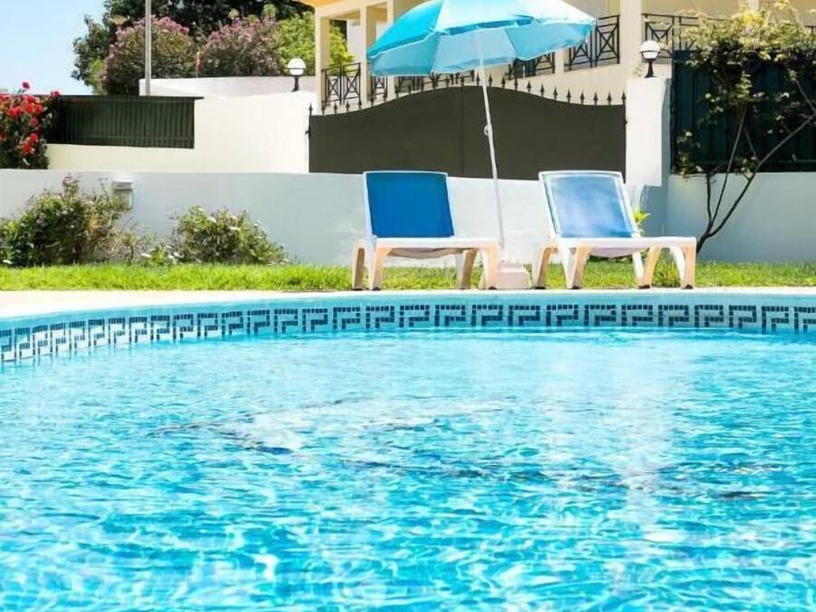 Una piscina con agua cristalina azul, rodeada de sillas de descanso y una sombrilla azul.