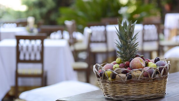 A wicker basket filled with fruits on a table in a dining area with white tablecloths and wooden chairs. - Hotel Funtana Noa (Villanovaforru)