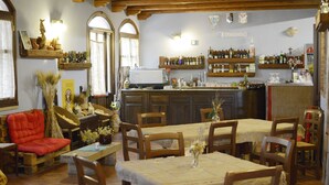 A cozy dining area with wooden tables and chairs, a bar with shelves of bottles, and a rustic decor with plants and a fireplace. - Hotel Funtana Noa (Villanovaforru)