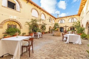 Un espace extérieur aménagé en terrasse, avec des tables et des chaises, entouré de plantes en pot et doté d’un sol en briques.