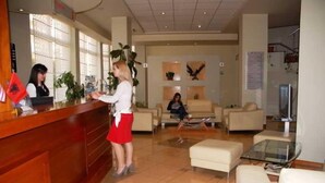 A reception area with a wooden counter, a receptionist, and a guest seated in the background. - Arvi (Durrës)