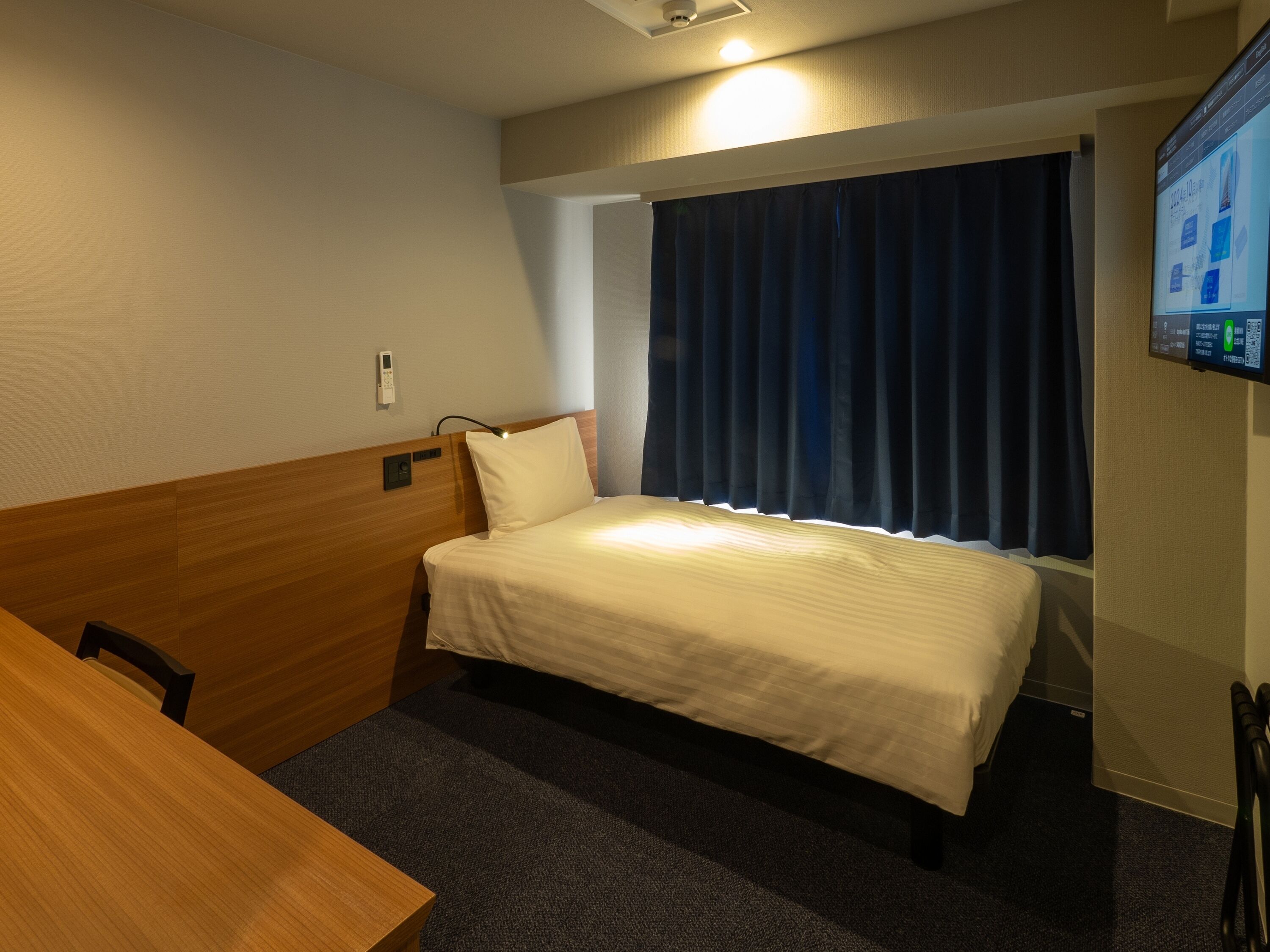 Habitación de hotel con cama, escritorio, silla, televisor y ventana con cortinas.