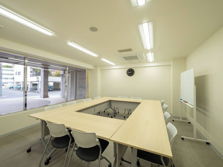 A conference room with a large table, four chairs, a whiteboard, and a clock on the wall.