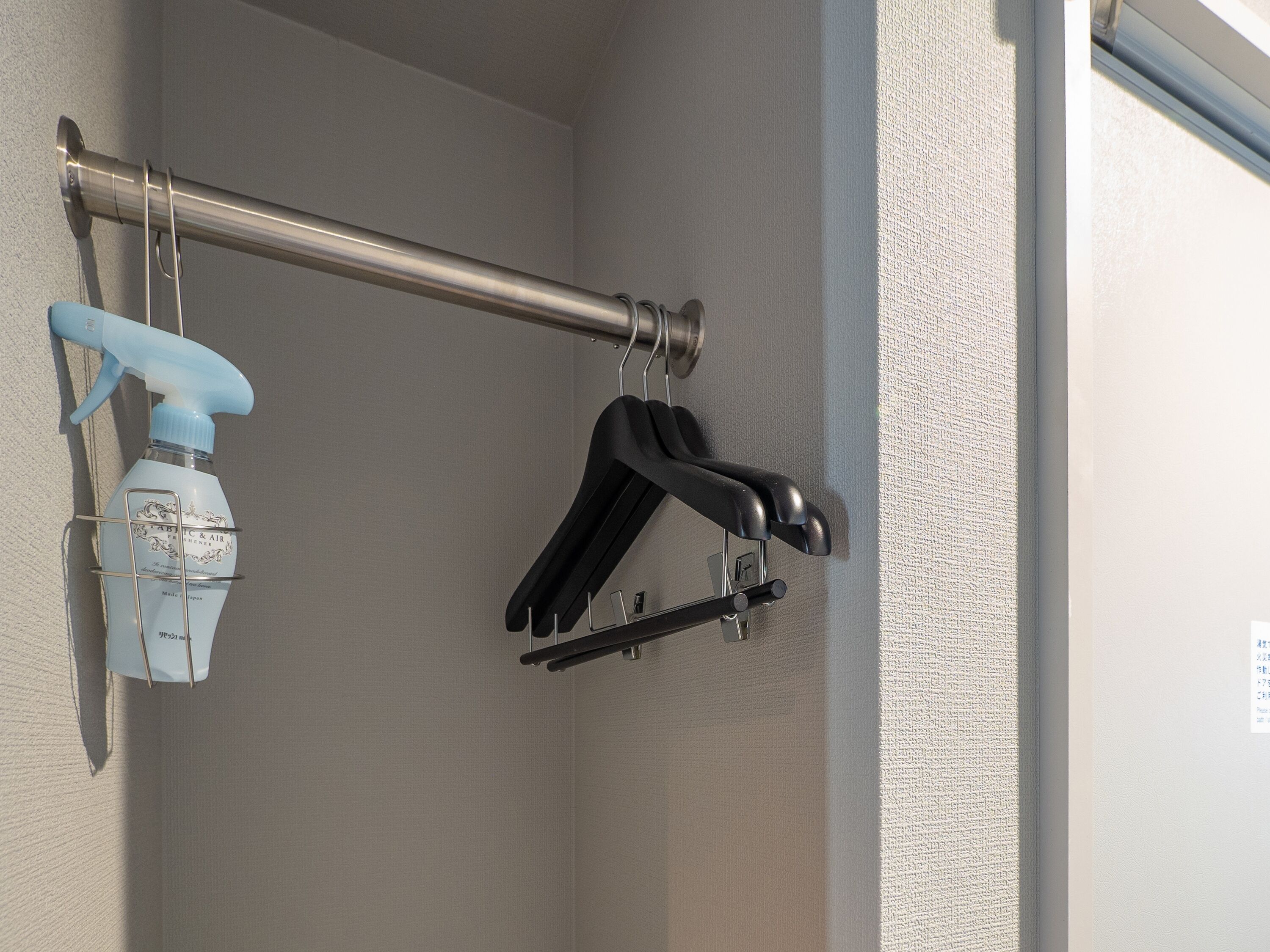A shower with a metal rod, a blue spray bottle, and black hangers.