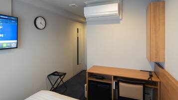 A hotel room with a bed, a desk with a chair, a small refrigerator, a wall-mounted clock, and a TV displaying a map.