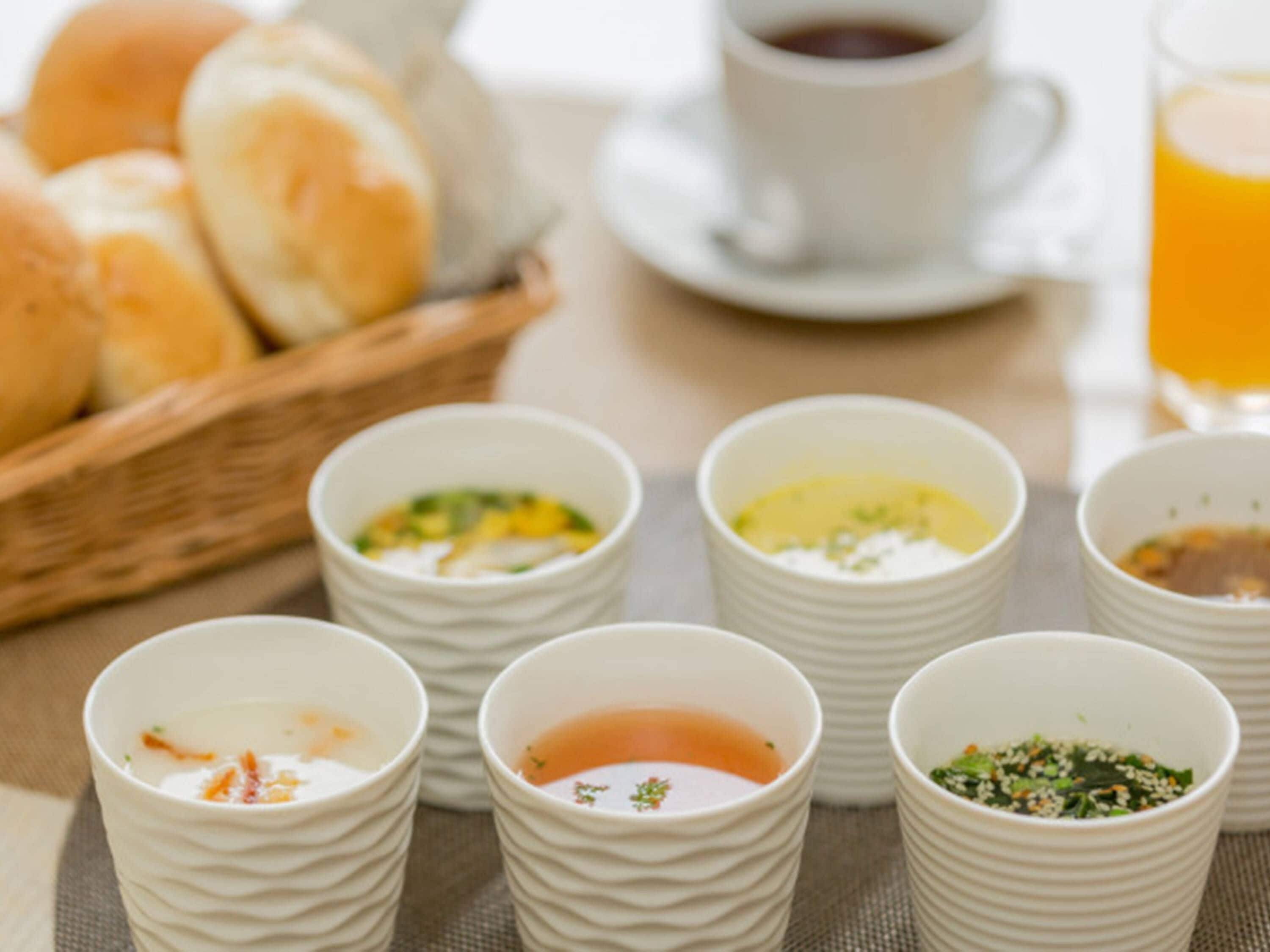A table with various food items and beverages, including bowls of soup, a cup of coffee, and a glass of orange juice.