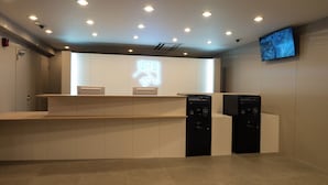 Ein Empfangsbereich mit Theke, einer Neonreklame, einem Wandfernseher und einer Überwachungskamera.
