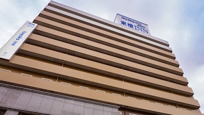 Ein mehrstöckiges Hotel mit modernem Design, das sich durch horizontale Linien an der Fassade auszeichnet und ein Schild mit der Aufschrift Toyoko Inn trägt.