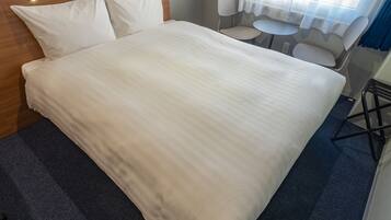 A neatly made bed with a wooden headboard, a small round table, and two chairs in a hotel room.