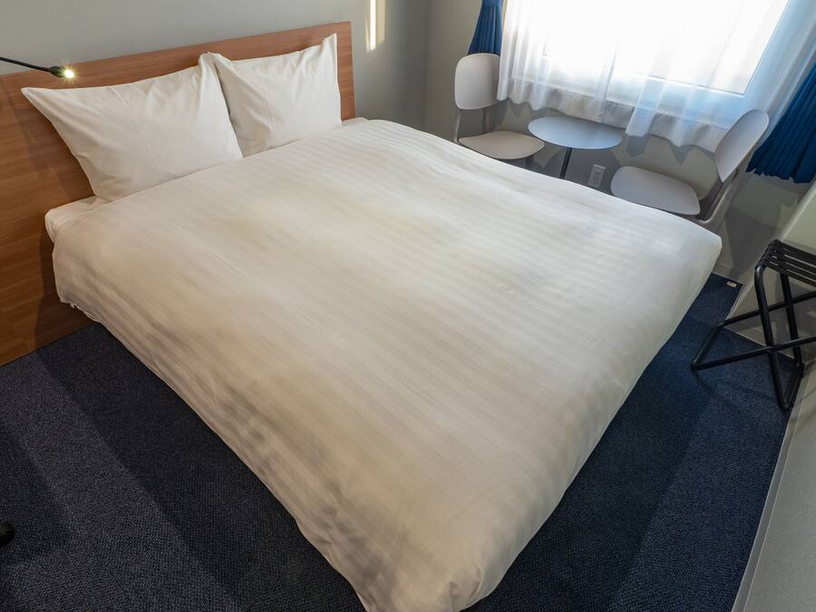 A neatly made bed with a wooden headboard, a small round table, and two chairs in a hotel room.