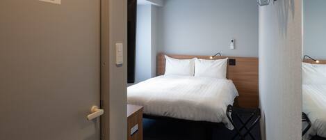 A hotel room with a bed, a bedside table, a wall-mounted light, and a ceiling vent.