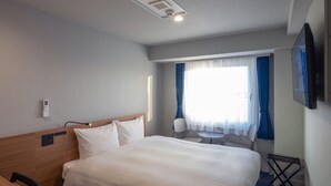 Ein Hotelzimmer mit Bett, Nachttisch, Stuhl, Fernseher und einem Fenster mit Vorhängen.