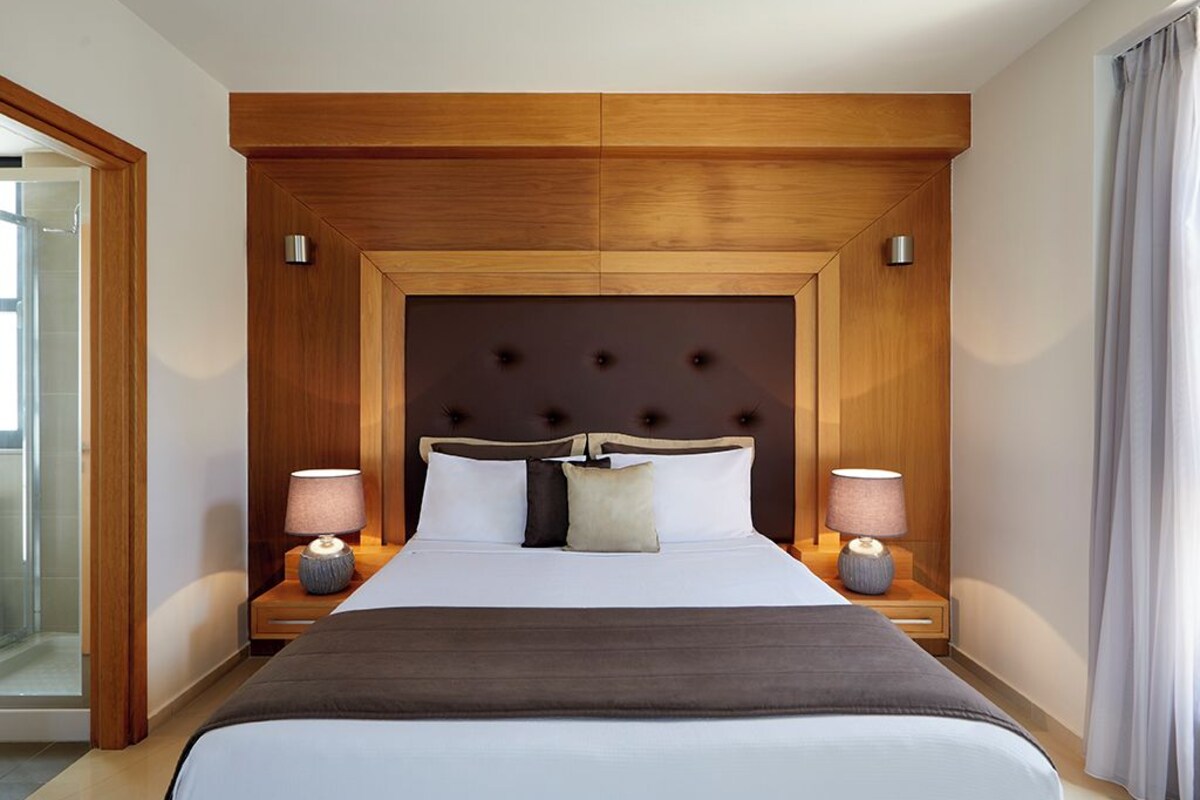 Ein Hotelzimmer mit einem großen Bett, einem Holzkopfteil, zwei Nachttischen mit Lampen und einer Duschkabine aus Glas.