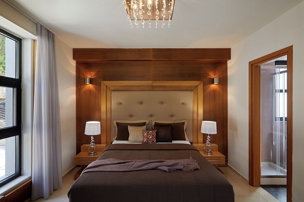 Ein Hotelzimmer mit einem großen Bett, einem Holzkopfteil, zwei Nachttischlampen und Blick aus dem Fenster.