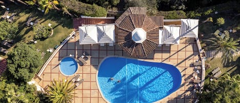 An aerial view of a resort with a large swimming pool, sun loungers, and umbrellas.