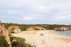 Ein Strand mit sandigem Ufer, blauem Himmel und ein paar Spaziergängern.