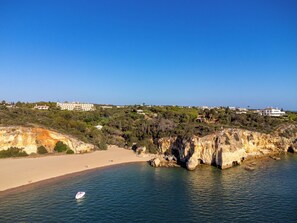 A coastal area with a sandy beach, rocky cliffs, and buildings in the background. - Casabela (Lagoa)