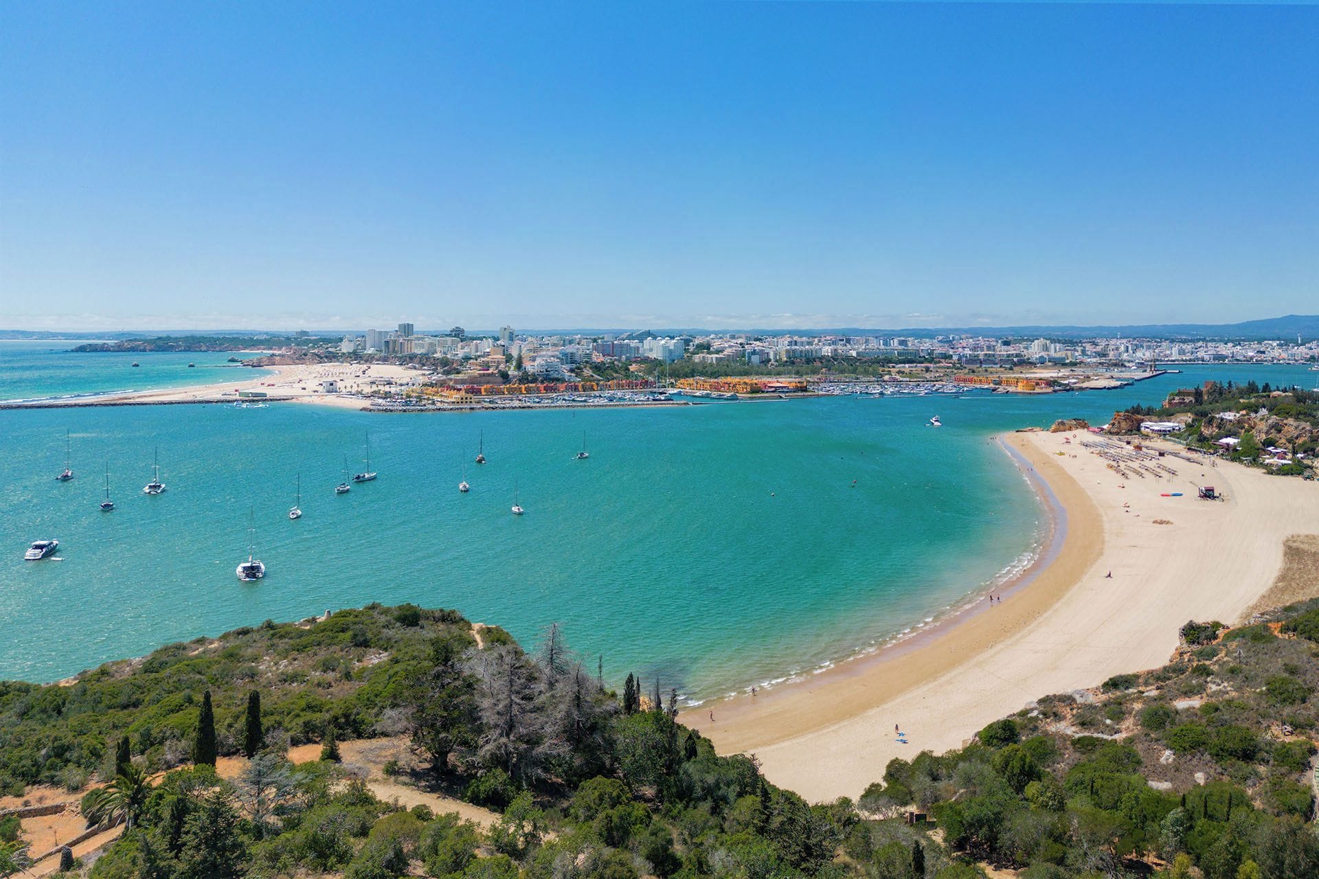 Eine Küstenstadtlandschaft mit sandigem Strand, Booten im Wasser und einer dicht bebauten Stadt im Hintergrund.